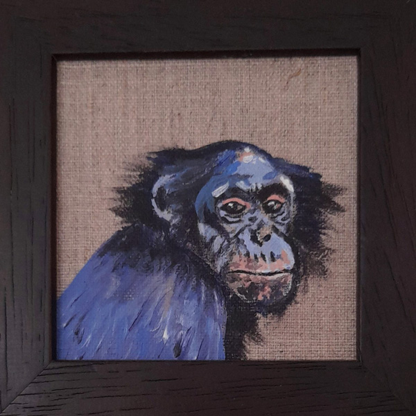 A painted monkey looks out of a wooden frame.