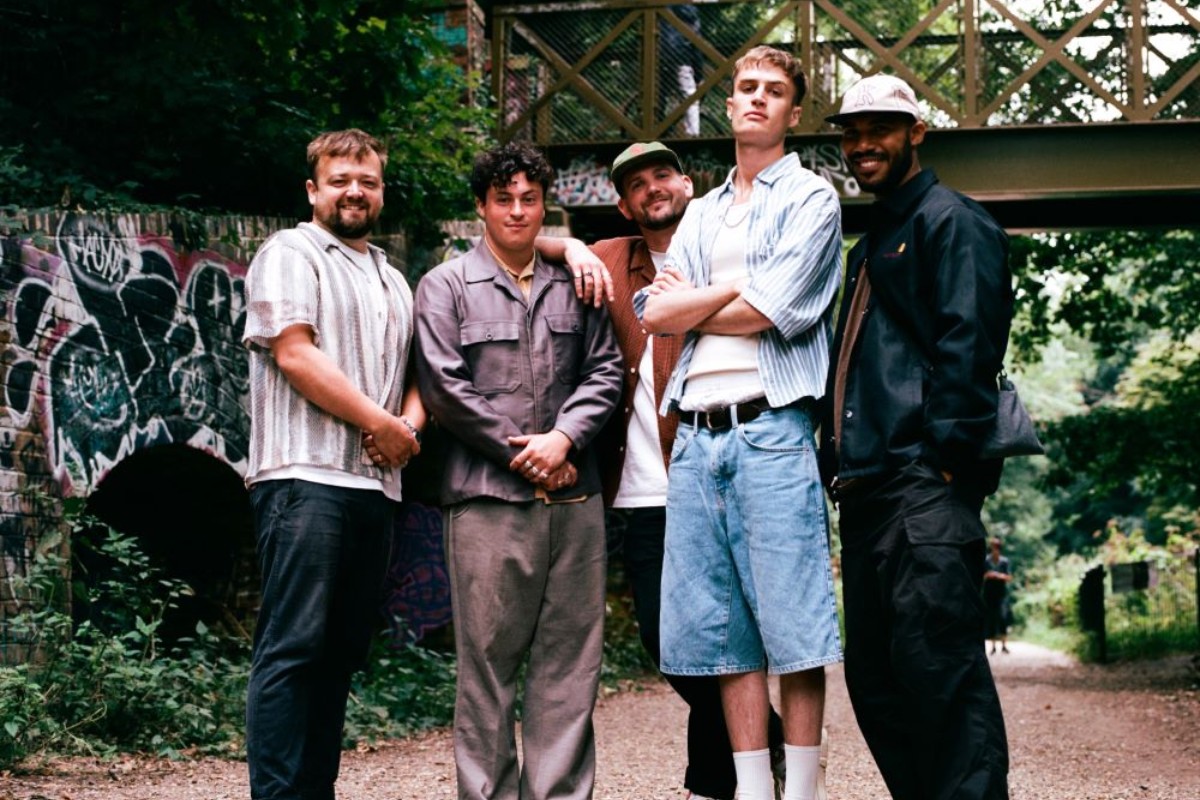 Kawala band stood on a pathway in front of an ironwork bridge